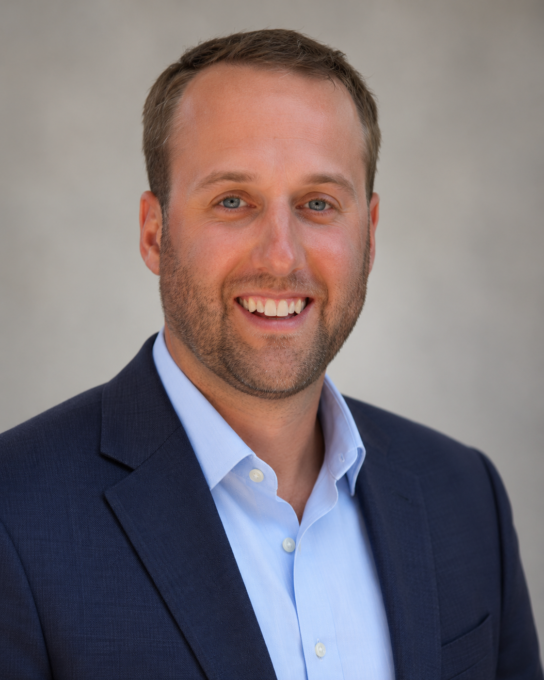 Portrait of Doug Woolley smiling in a navy blazer and light blue shirt