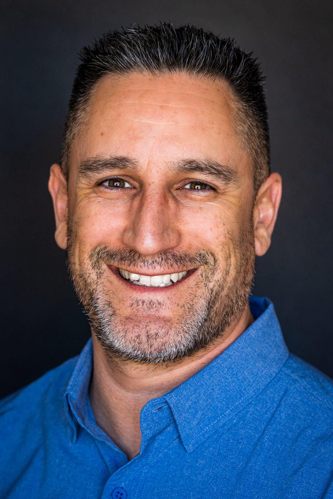 Portrait of Raul Vasquez smiling in a blue shirt against a dark background